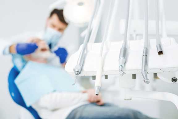 پزشک در حال معاینه بیمار در کنار ابزار دندانپزشکی